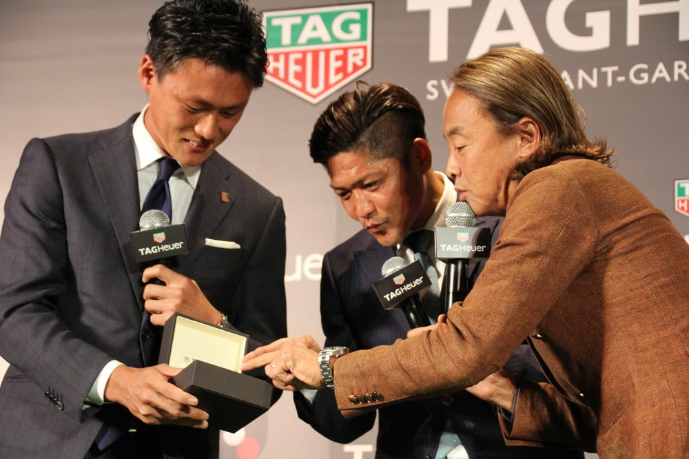 タグ・ホイヤーの最新モデルの腕時計を持つ李忠成（左）と、興味深く見つめる大久保嘉人（中）、北澤豪