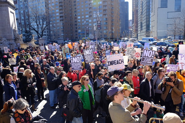 愛国歌「アメリカ・ザ・ビューティフル」を歌う人たち。大勢の反トランプ派に交じり、
左後方に「BUILD THE WALL」のボードを持ったトランプ派も見える。