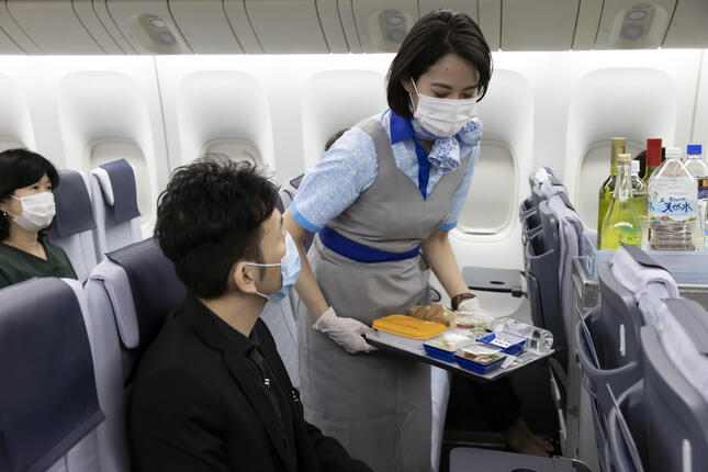 ANAの客室乗務員は機内でマスクとビニール手袋を着用し、機内食などをトレーに載せて提供している（ANA提供）