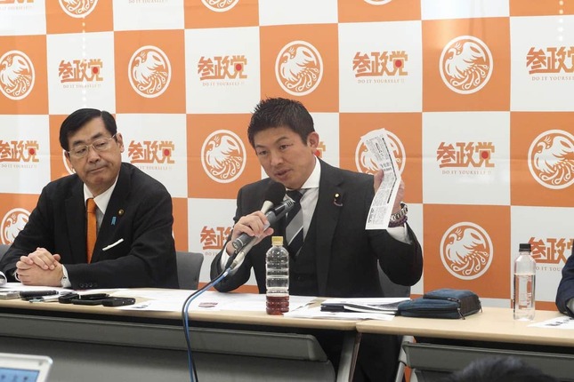 「なりすましビラ」事案を報じた西日本新聞の記事を手に説明する参政党の神谷宗幣副代表（参院議員）。写真左は松田学代表