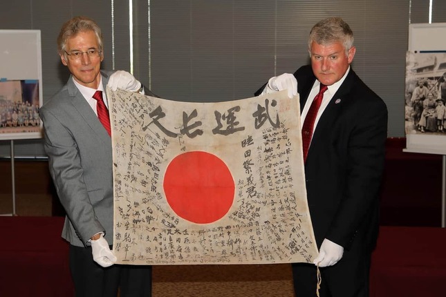 陸田繁義さんの遺品の日章旗を披露する「OBONソサエティ」のレックス・ジーク共同代表（左）とUSSレキシントン博物館のスティーブ・バンタ館長（右）