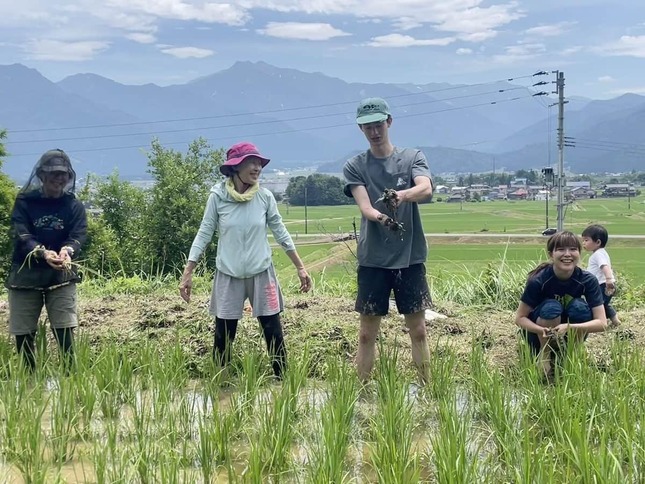 2025年6月22日、大前さんたちは田んぼの草取りに出かけた。30度を超す暑さだが、田んぼに足を入れると冷やりと気持ちが良い。後ろに見えるのが巻機山