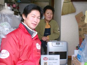 宮城県松島町の高田さん。海沿いにあったご自宅には津波が押し寄せ、今は更地だといいます。「寒くなってきたのにエアコンの調子が悪く、ファンヒーターは助かります。」（2011年12月22日、左は難民を助ける会仙台事務所の小菅健太郎）