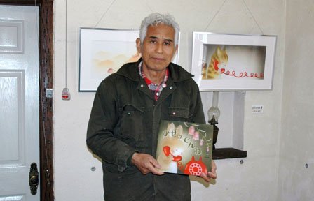 展示されている原画を前に絵本を手にする佐々木格さん＝2014年4月20日、大槌町吉里吉里