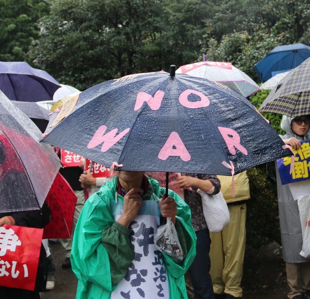 「NO WAR」と書いた傘を差す女性