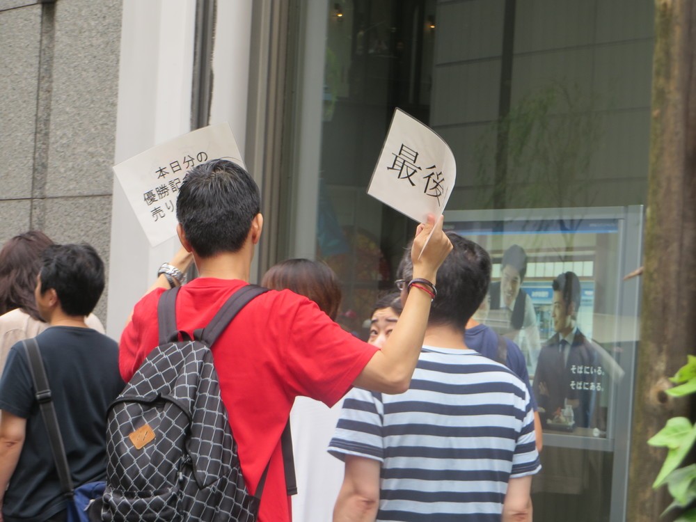 「最後尾」と「グッズ売り切れ」を掲げるスタッフ