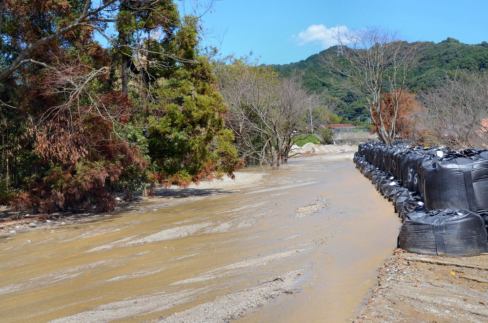 川の水はいまだに濁った色のまま。水害対策に土嚢が積まれていた
