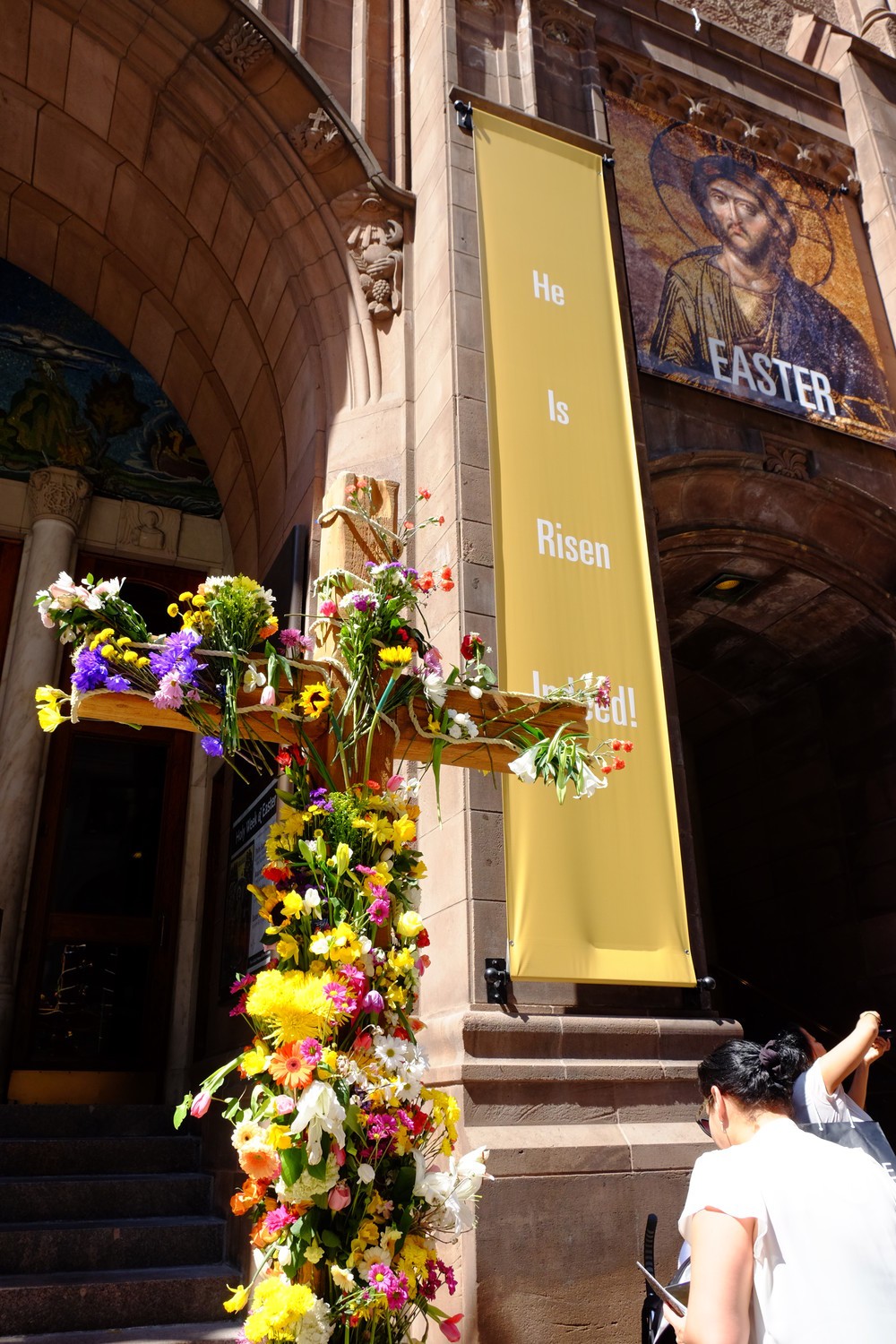2017年の復活祭の日。ニューヨーク市マンハッタンの五番街の教会前に大きな十字架が掲げられ、道行く人々に配られる生花が飾ってあった