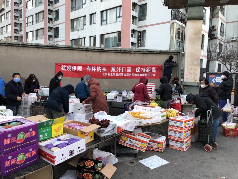 北京市内の団地の前で野菜の行商をする人たち。壁に掲げられたスローガンは「マスクをかけ、人との距離を保とう」（2020年2月24日）