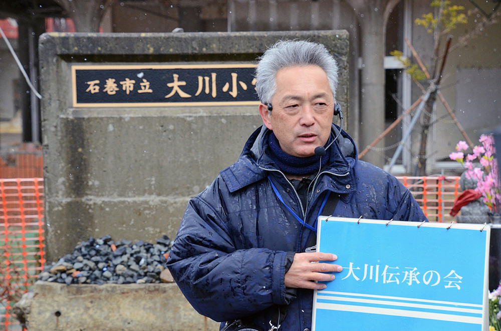 雪が舞う中、大川小学校で語り部をする鈴木典行さん