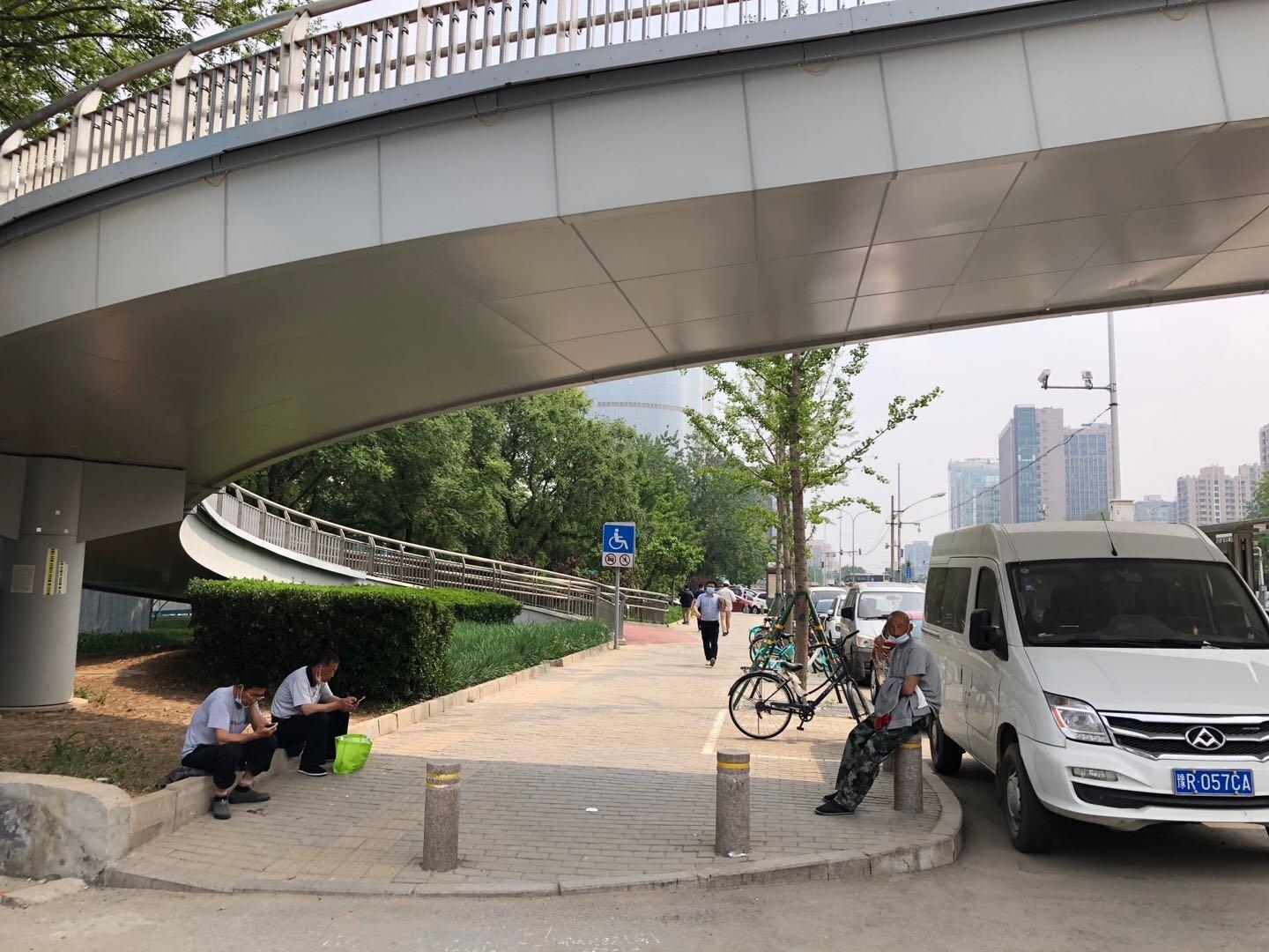 北京市内の「首都体育館」近くの横断歩橋橋の下で涼を取る出稼ぎ労働者たち。コロナショックの前は多くの労働者が群がっていたが、現在は人影もまばらだ（2020年5月6日、筆者撮影）