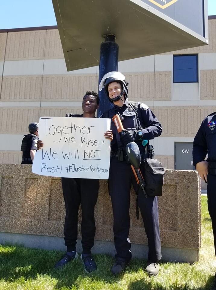 「我々はともに立ち上がる」という紙を掲げて白人警官と写真に収まる黒人デモ参加者（Colby Warzechaさん撮影・提供）