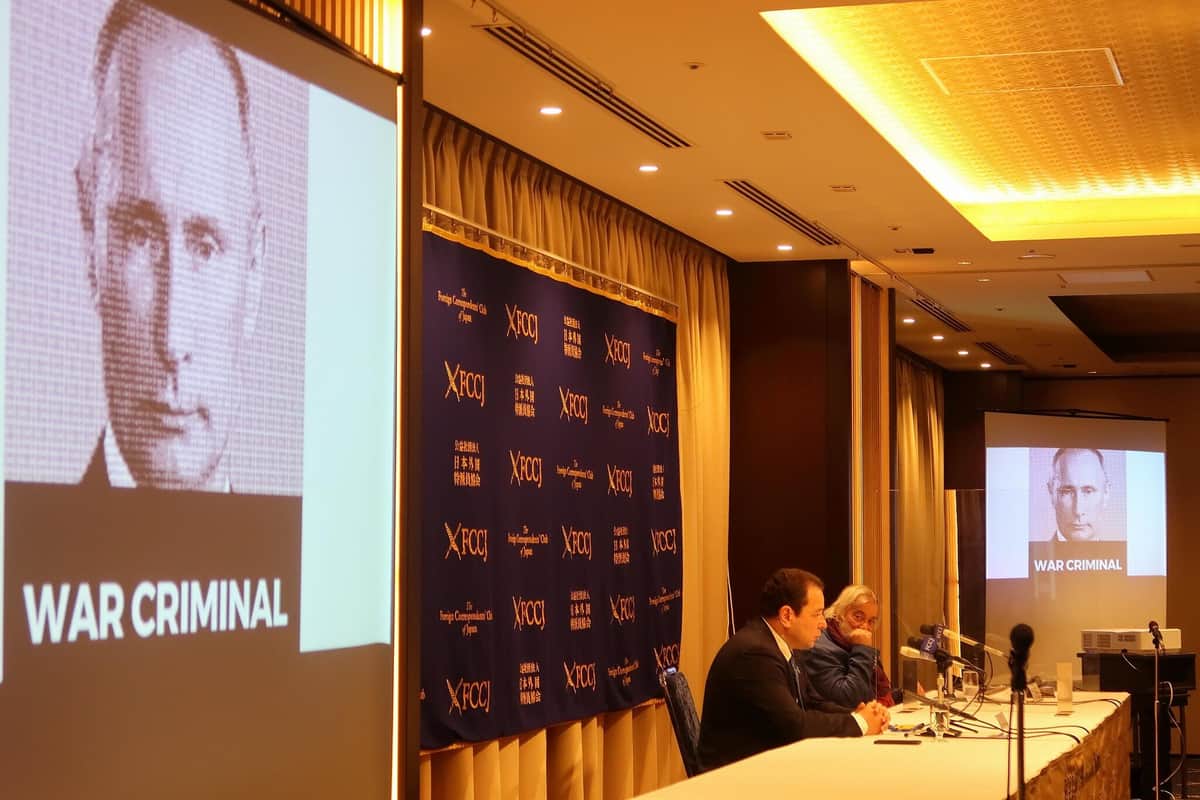日本外国特派員協会で記者会見するウクライナのセルギー・コルスンスキー駐日大使（手前）。ロシアのプーチン大統領に「戦争犯罪人」の文字が入ったスライドを映しながら、ロシアの侵攻を非難した