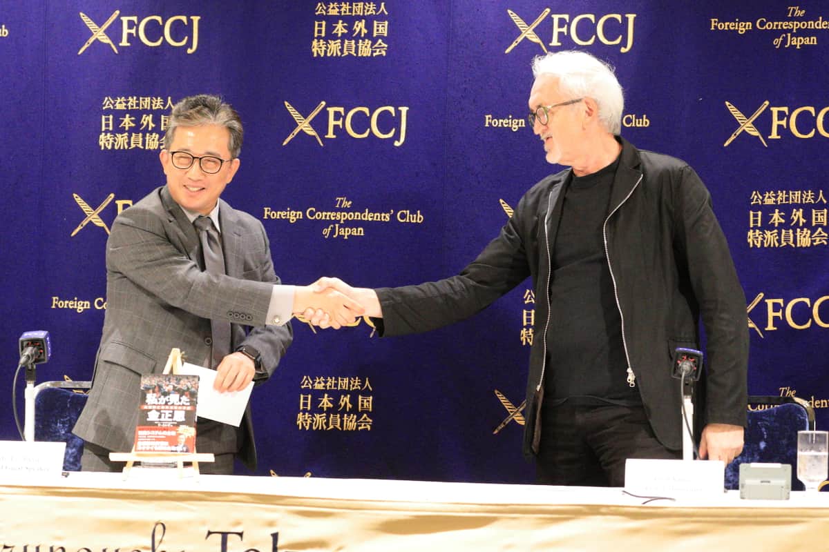 記者会見が終わると司会者と笑顔で握手
