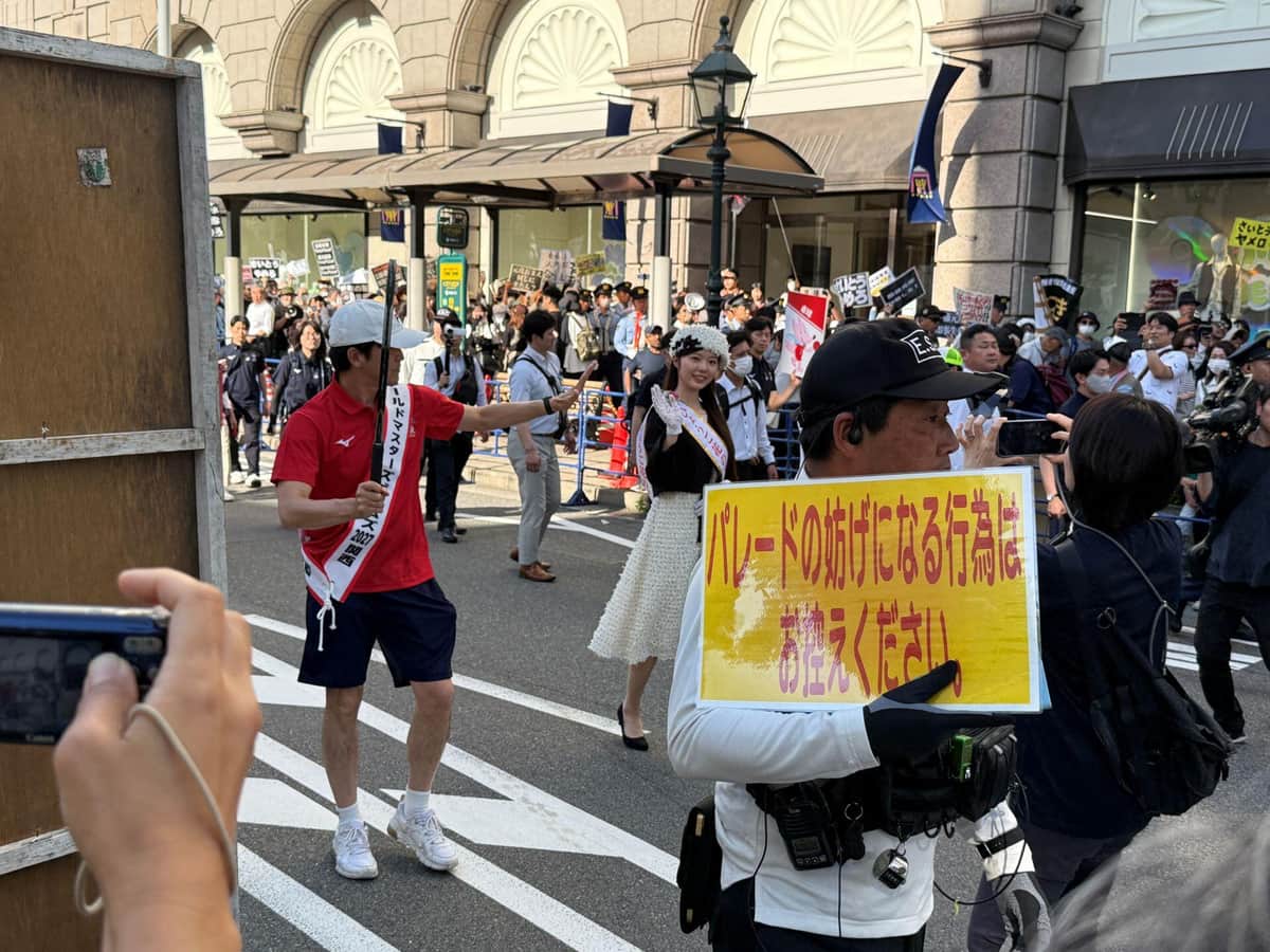 「パレードの妨げになる行為はお控えください」とプレートを掲げる警備員（右）（5月17日、神戸市中央区）