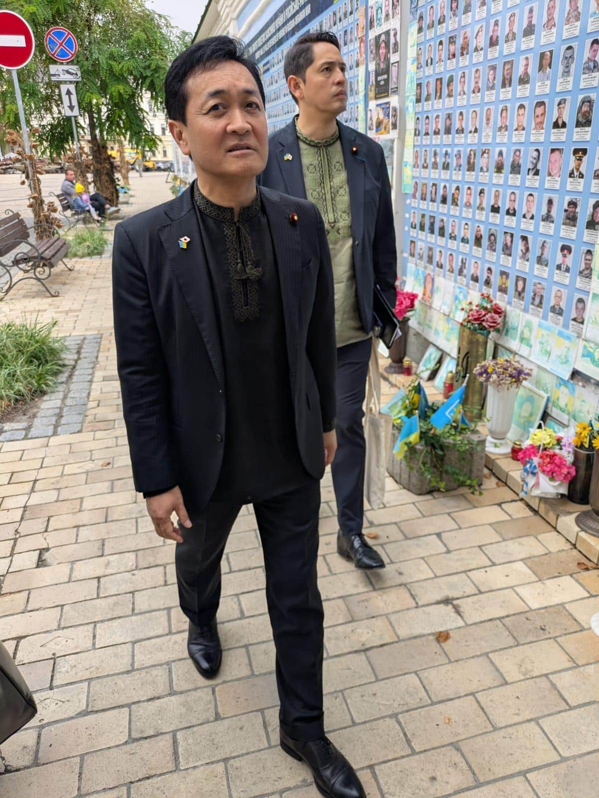 ウクライナの民族衣装・ヴィシヴァンカを着用した国民民主党・玉木雄一郎代表（手前）と深作ヘスス衆院議員（奥）。壁一面に並ぶ兵士の遺影と献花が、長期化する戦争の犠牲の大きさを示している（写真提供：深作ヘスス事務所）
