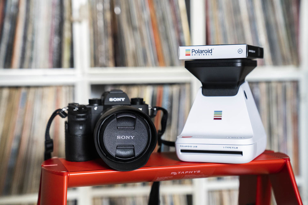 【写真左】デジタル一眼レフカメラ、ILCE-9　α9（ソニー）。フルサイズ（35mm）のCCDを搭載したミラーレス一眼カメラ、αシリーズの最高峰モデル。【写真右】スマートフォン用暗室（フォトプリンター）、Polaroid LAB（Polaroid Originals）。スマートフォンやタブレットに保存されているデジタル画像を、フィルムに投影することで、ポラロイド写真として現像できるユニークなデバイス。