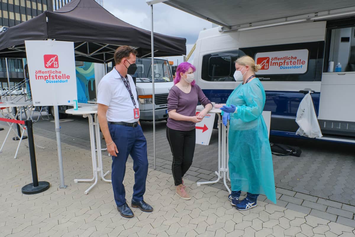 ドコミのワクチン会場を視察するデュッセルドルフ市ブルクハルト・ヒンチェ危機管理部長と、ドコミ参加者ケリー・ジンデマンさん、内科医のグニラ・エアドマンさん。
（c） Landeshaupstadt D?sseldorf/Michael Gstettenbauer