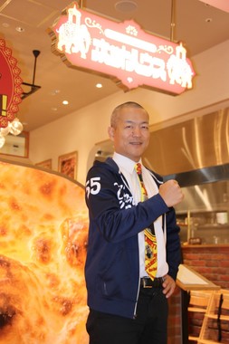 「ゴーゴーカレー」に続くブランド「ホットハウス」の店舗前で、「55」と記されたパーカーを切る宮森CEO