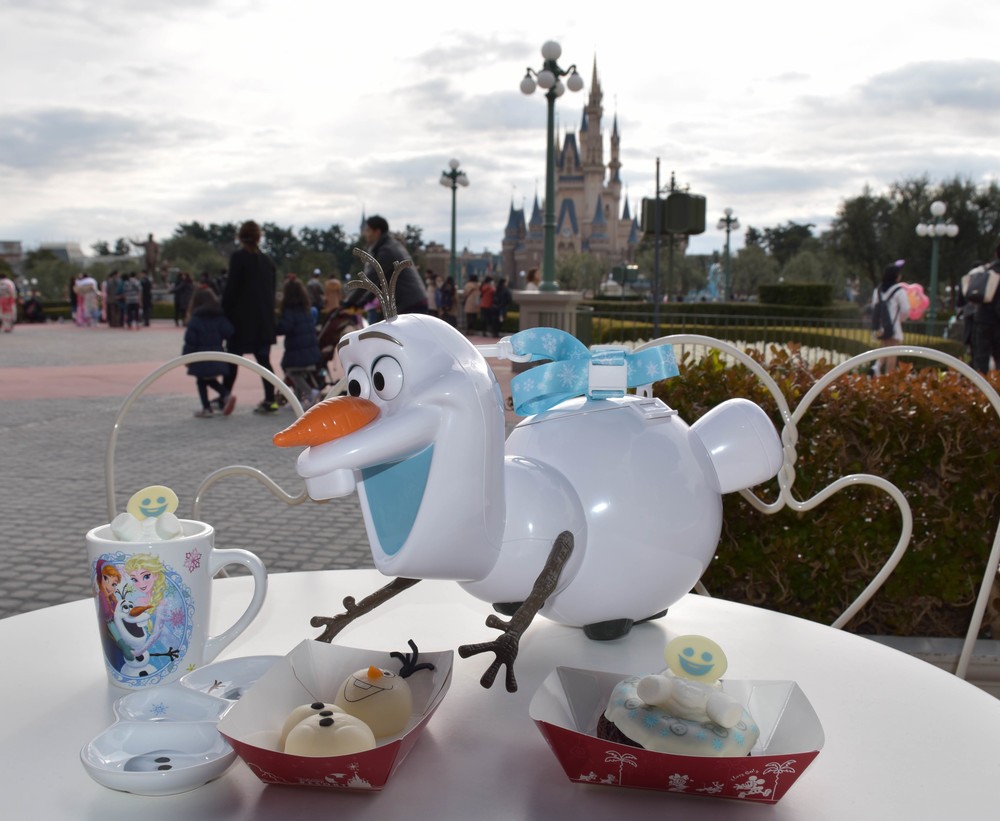 オラフをモチーフにしたバケット付きポップコーン(中央)や、スーベニアカップ付きオレンジ風味ミルクムース(左)、スーベニアプレート付きオラフもち(手前中央)、ベイクドチョコレートドーナツ(手間右)