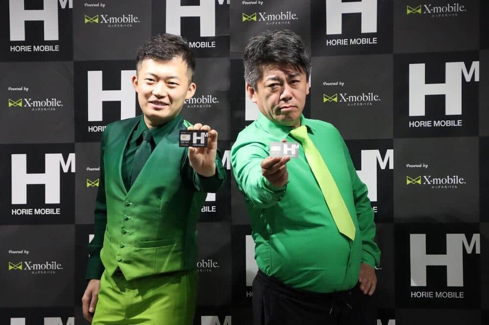 「HORIE MOBILE」のSIMカードを手に取る堀江貴文氏（右）　左はエックスモバイル代表木野将徳氏